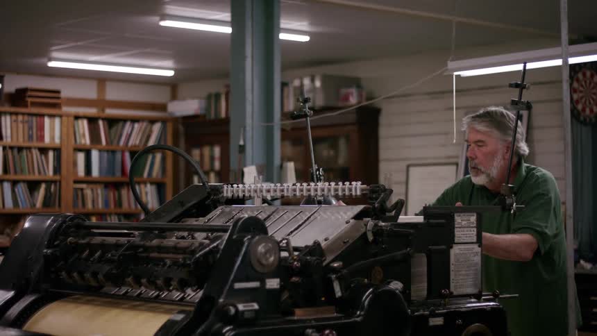 A man operates a large vintage printing press in a workshop