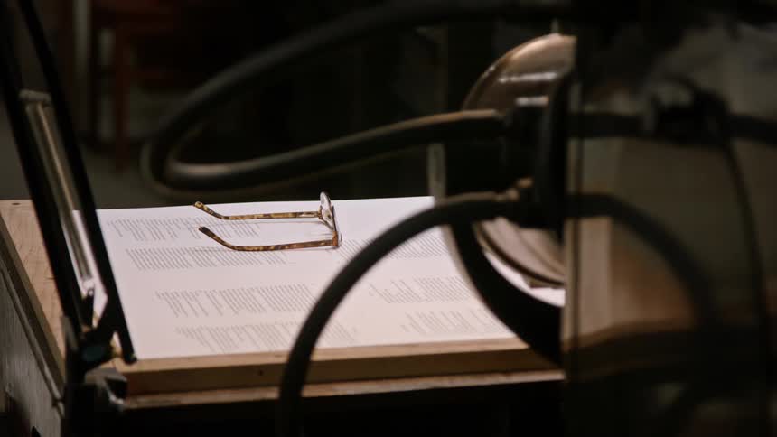 Reading glasses on top of a printed page of paper next to a printing press indoors