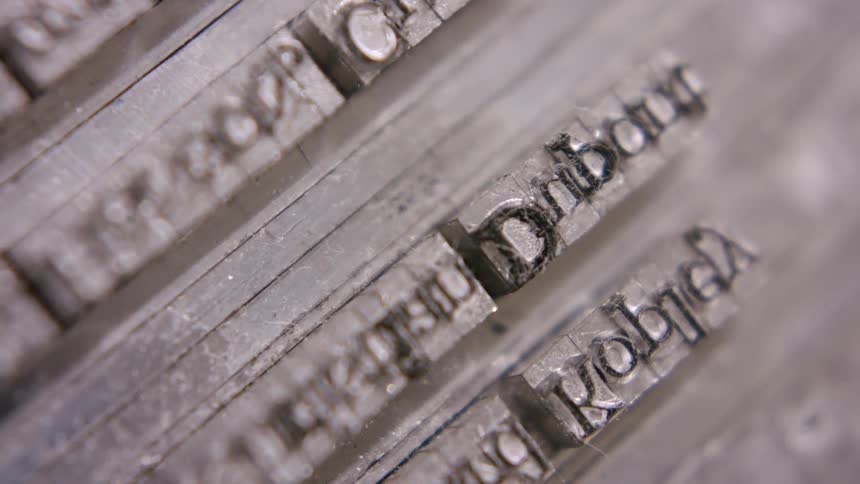 A close view of several rows of silver metal movable type letters arranged backward and upside down with a soft focus on the details of the lettering