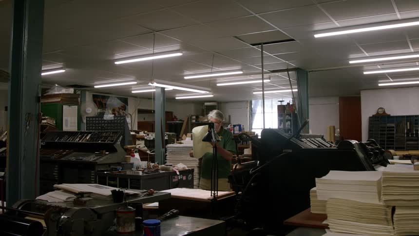 Bearded man inspecting paper coming out of a printing press indoors during day time