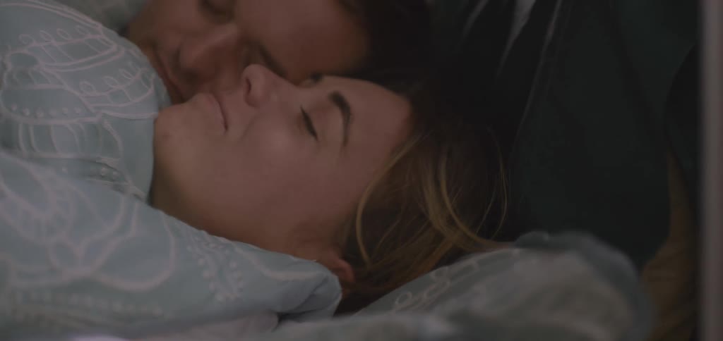 A couple is shown lying in bed snuggling close together the shot is a closeup focusing on their faces as they appear to be sleeping peacefully