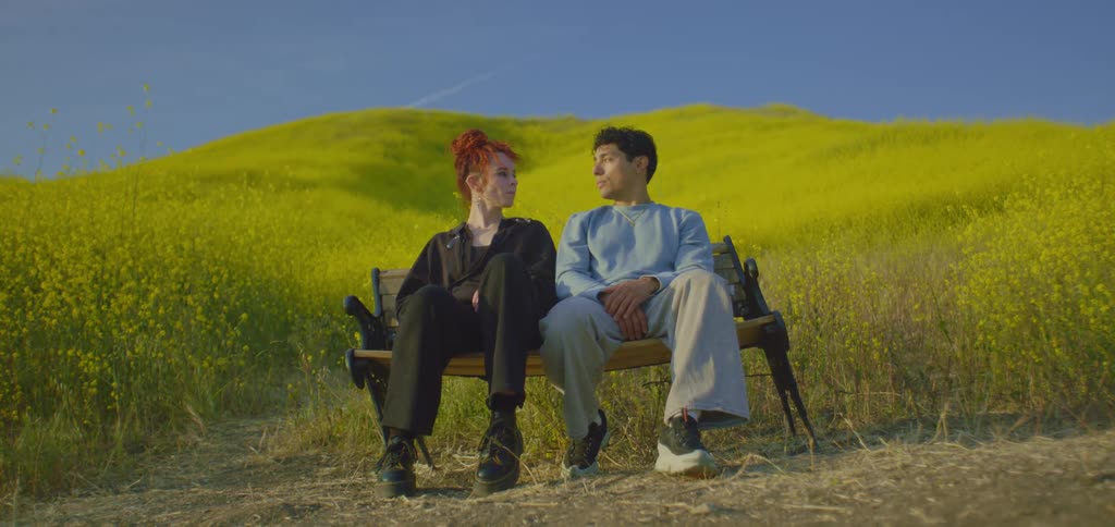 Man and woman sitting on a bench at the base of a flower covered hill nod at each other before standing
