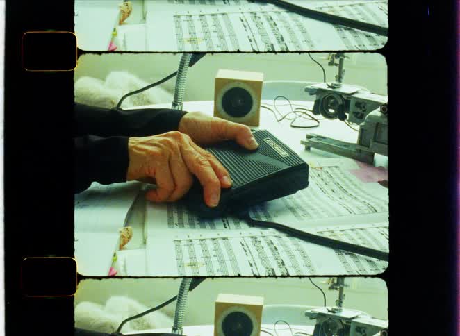 Hand rests on a control pedal over a table covered with musical scores and audio equipment