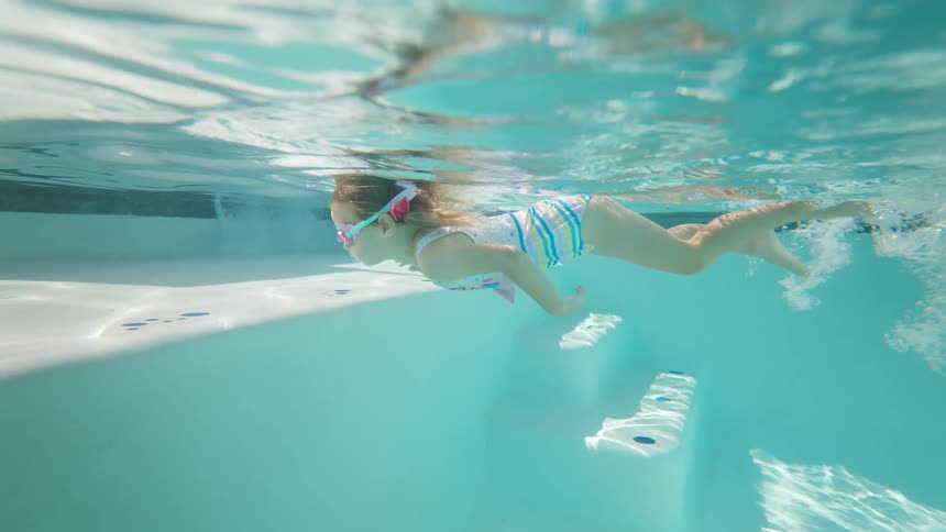 Girl swims underwater toward the pools edge wearing pink goggles