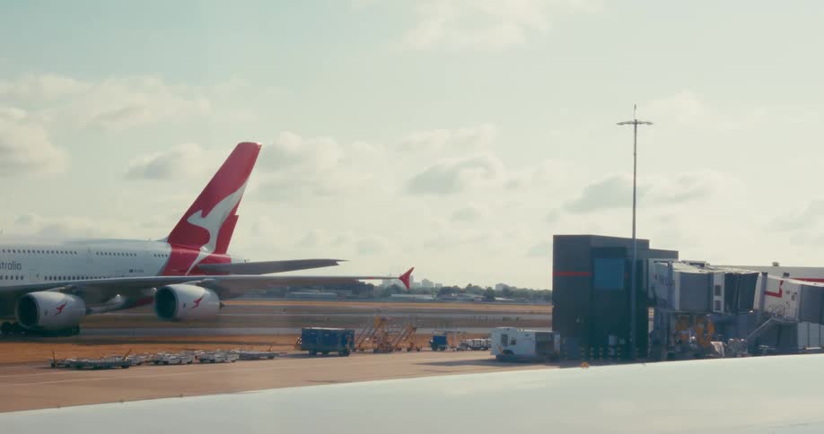 A large airplane sits on an airport tarmac near a gate and there are airport vehicles around it