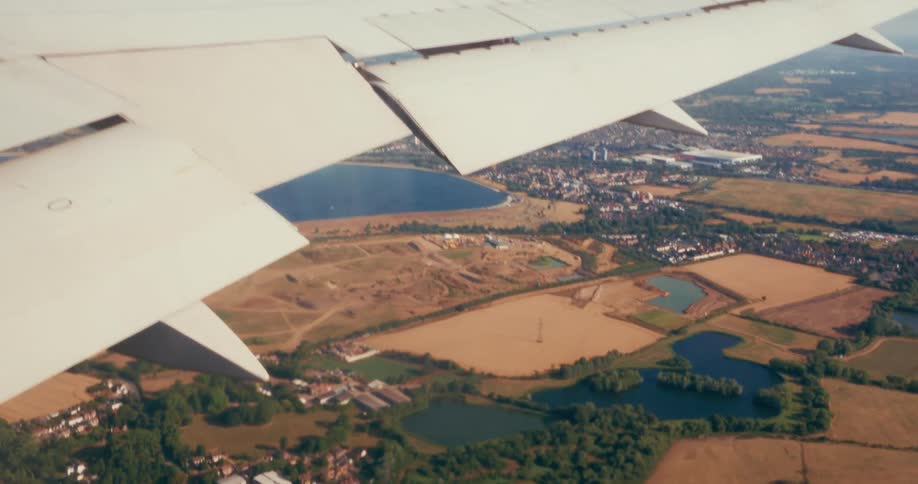 Airplane wing flying over rural and urban areas with lakes and fields