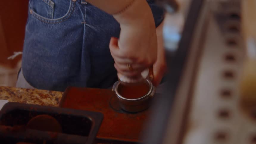 Person tamps coffee grounds in the portafilter before making espresso