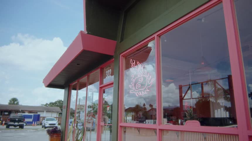 The video shows an exterior shot of a building with large windows and a red awning a bicycle some plants and a sign with a number are visible on the exterior wall