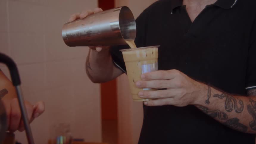 A barista pours a shaken drink into a cup behind the counter