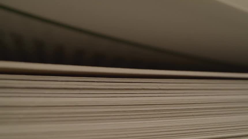A close view of the side of a large stack of light colored papers is shown as the pages appear to be slowly fanned out