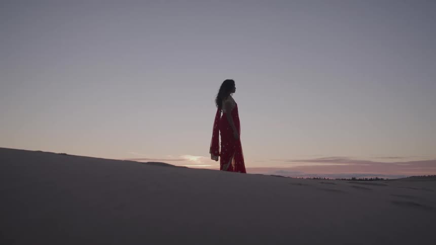 Woman in a red dress walks across the dunes at sunset