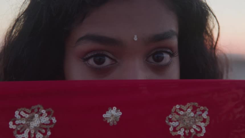 Expressive eyes of a woman above a red fabric embroidered with golden details