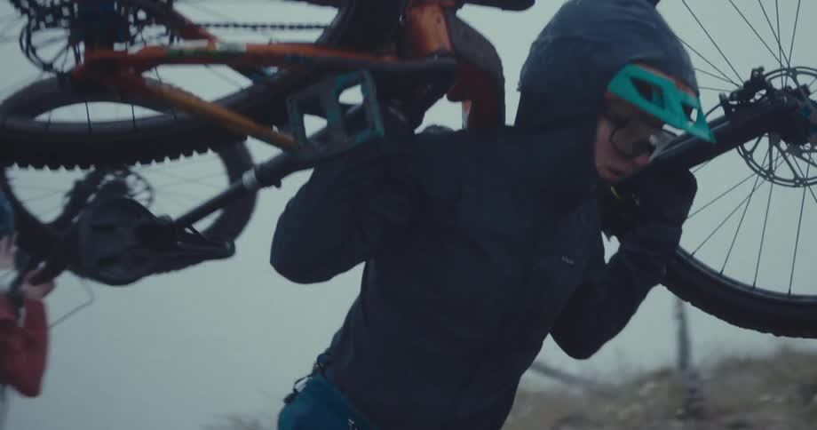 Two female cyclists carry their bicycles up a frost covered slope on a foggy day