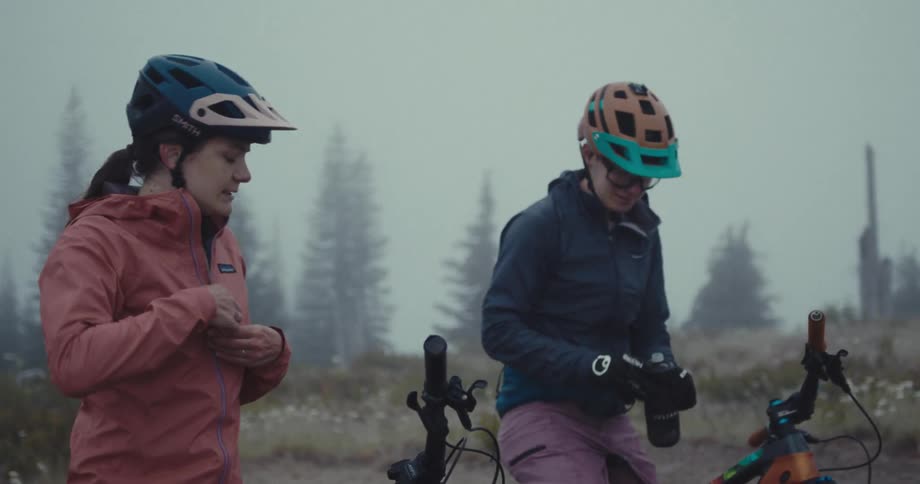 Two cyclists rest in a foggy forest with one sipping from a bottle