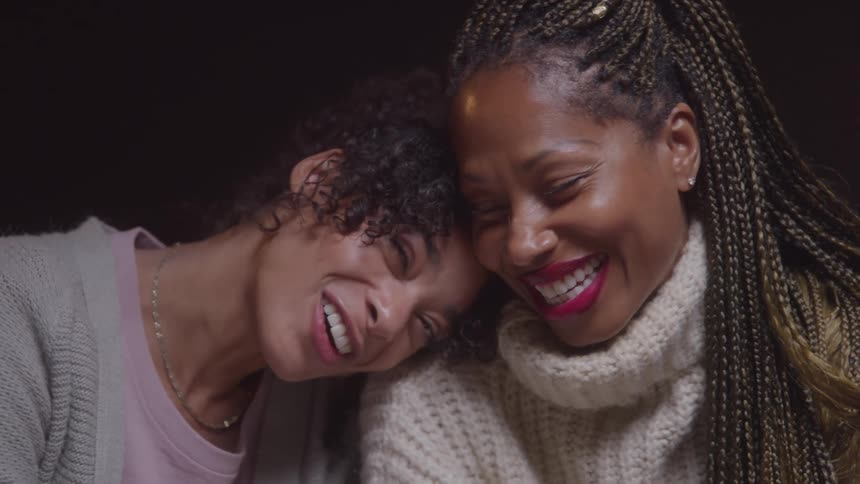 Two women smile with their heads leaning together in an affectionate gesture