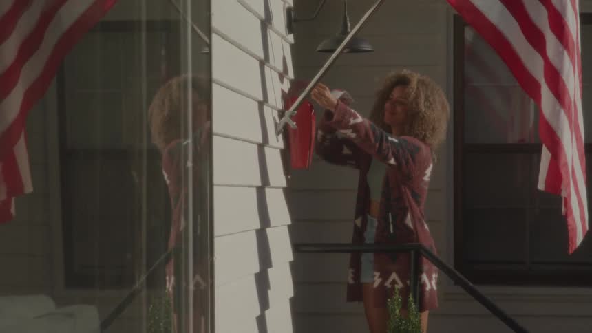 A woman walks to a mailbox on a wall opens the mailbox takes out some mail and walks away