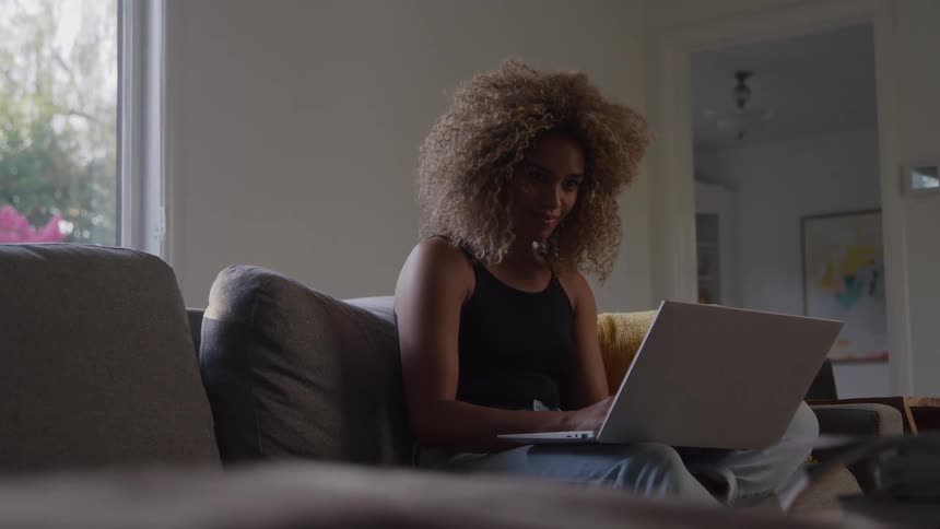 A black woman sit on a couch while using her laptop computer