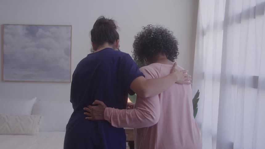 The video shows a man and a woman standing in a bedroom with the woman facing away from the camera the man has his arm around her and she has hers around his back