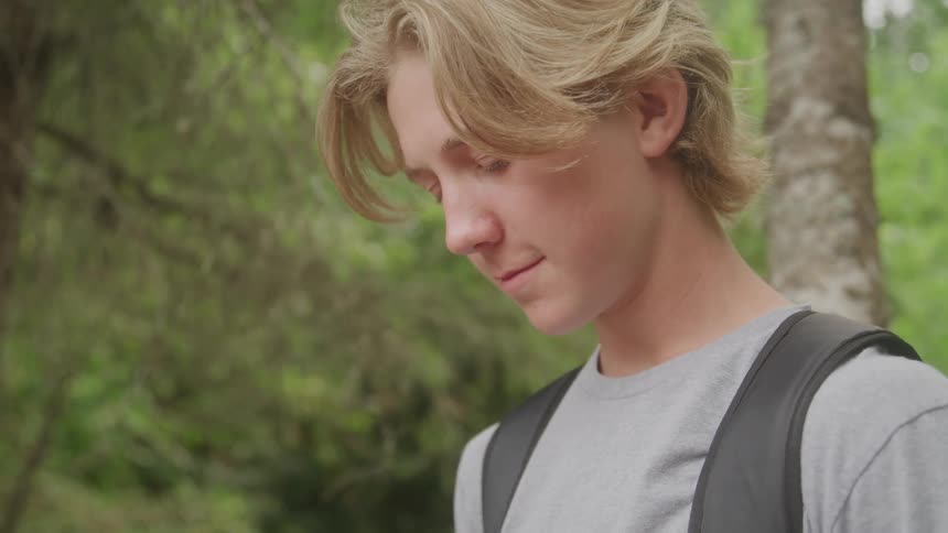 Young man with a backpack looks down amidst the greenery
