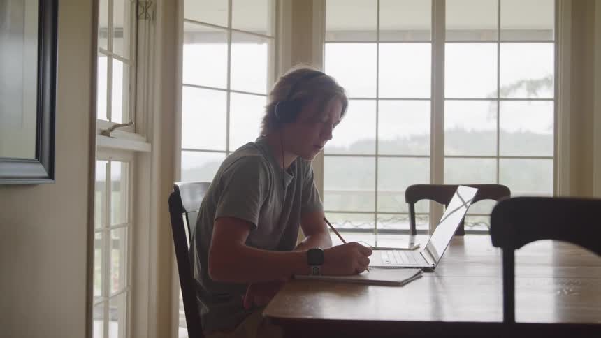A teenage boy sits in the dining room while doing homework