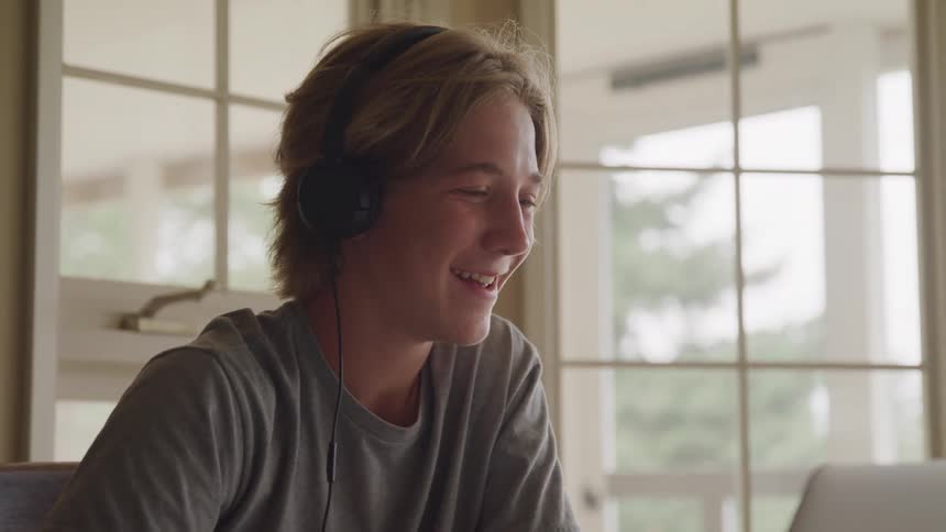 Smiling young person wears headphones while looking ahead in a room lit by glass windows