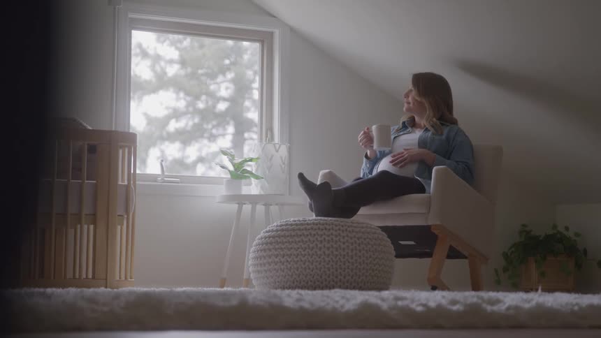 A pregnant woman sits in a chair holds a cup and touches her belly