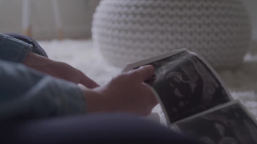 A person holds and flips through ultrasound pictures while sitting on a soft carpeted floor