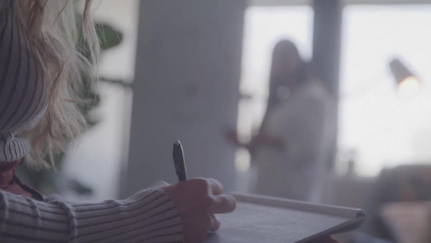 A hand takes notes while someone speaks offscreen