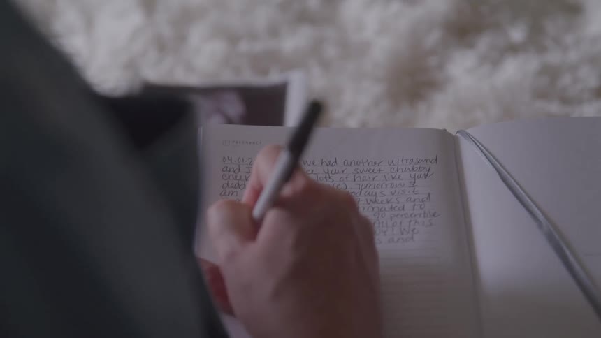 A hand holds a pen and writes in a notebook