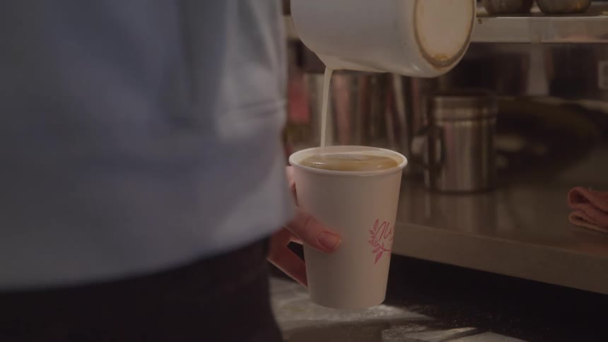 A barista pours steamed milk into a coffee cup in a cafe