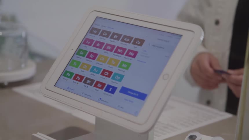 A hand selects options on a pointofsale tablet at a counter colorful buttons reflecting under shop lights