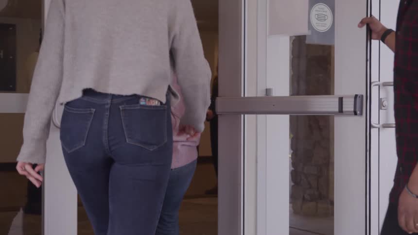 People enter through a glass door as someone holds it wide