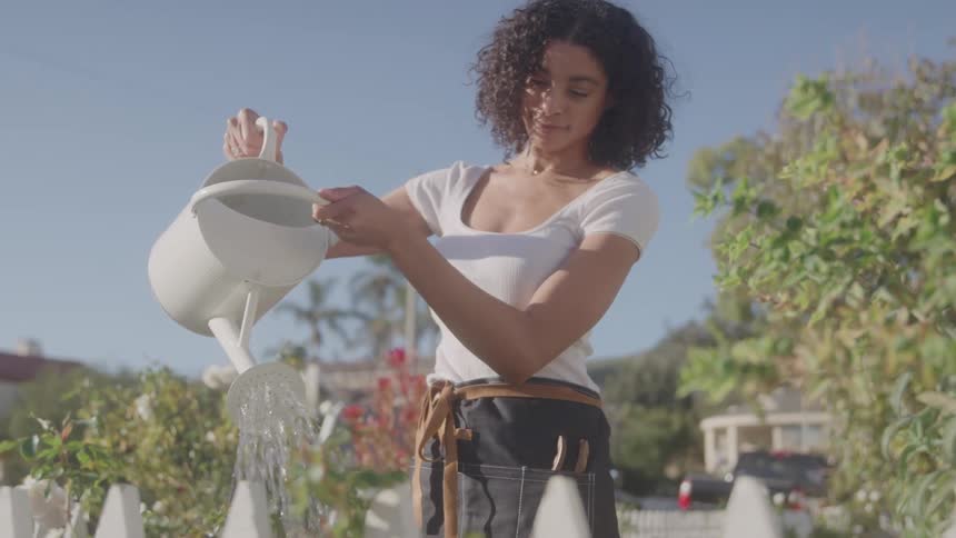 A woman watering the plants in her garden on a sunny day