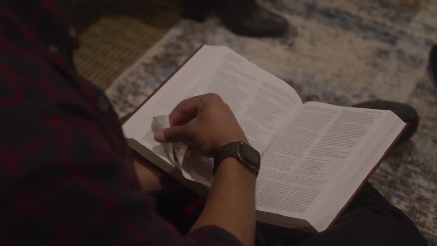 Someone studies an open book on their lap hands turning pages