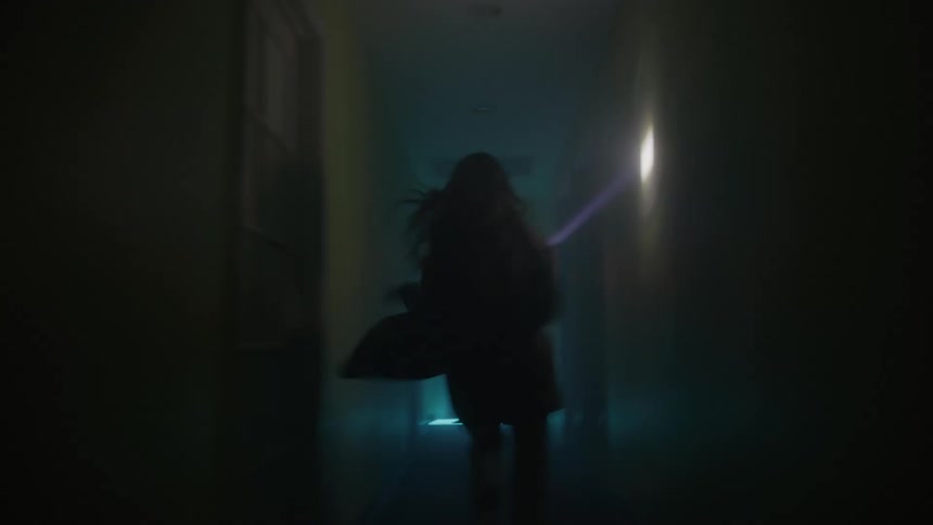 A woman running away from something heading down a corridor with only her flashlight chaotically lighting her way