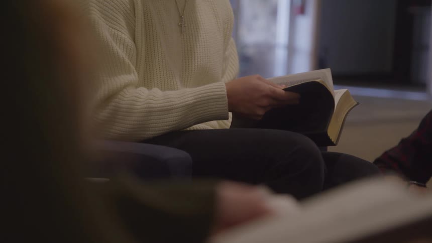 A small group of people are seated thumbing through books as a black male smiles