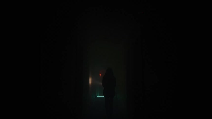Silhouette of a young woman walking through a dark corridor with a torchlight at night