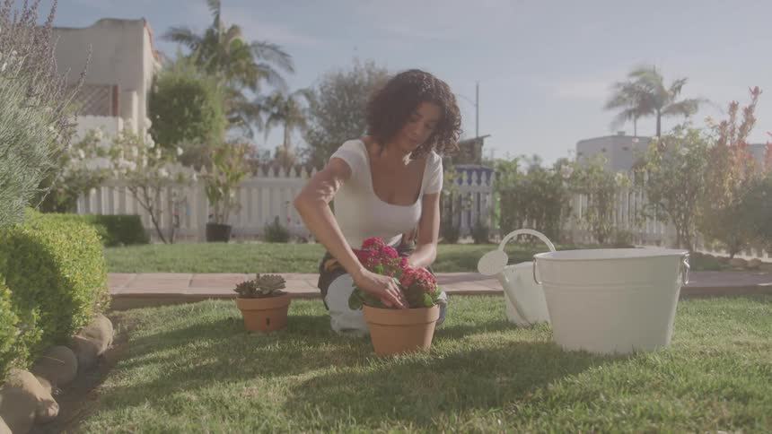 A woman kneels in her garden planting flowers in a pot