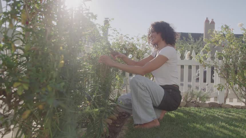A woman tends plants in a garden under a bright sun