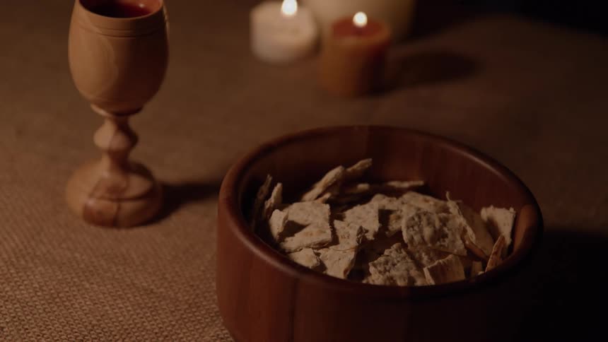 Hand reaches into a bowl of communion wafers by a chalice and candles