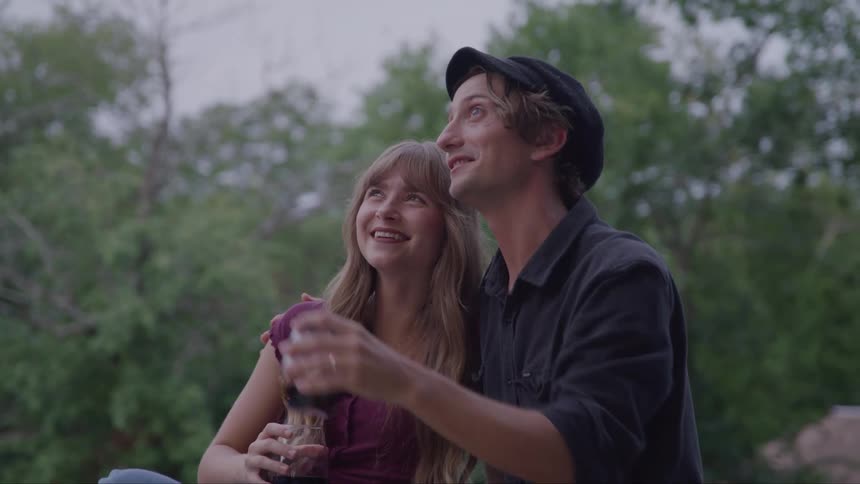 A happy couple relaxes outdoors with wine sharing a light moment beneath soft dusk light