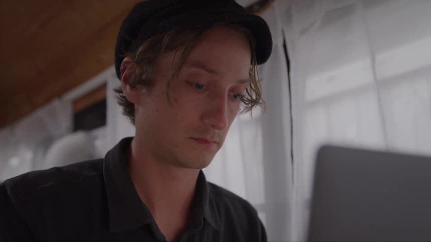 Close up of a young man using a laptop while sitting down in a room during daytime