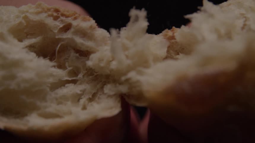 A person holding a piece of bread pulls it apart into two halves