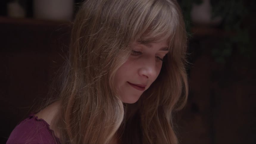 The video shows a closeup shot of a woman with long blonde hair looking down with a gentle smile on her face her head is tilted slightly and she appears content