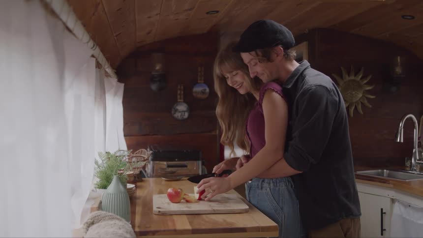 A couple embraces while slicing an apple in a cozy wooden kitchen