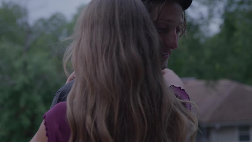 In an outdoor setting a woman wraps her arms around a man as they slow dance