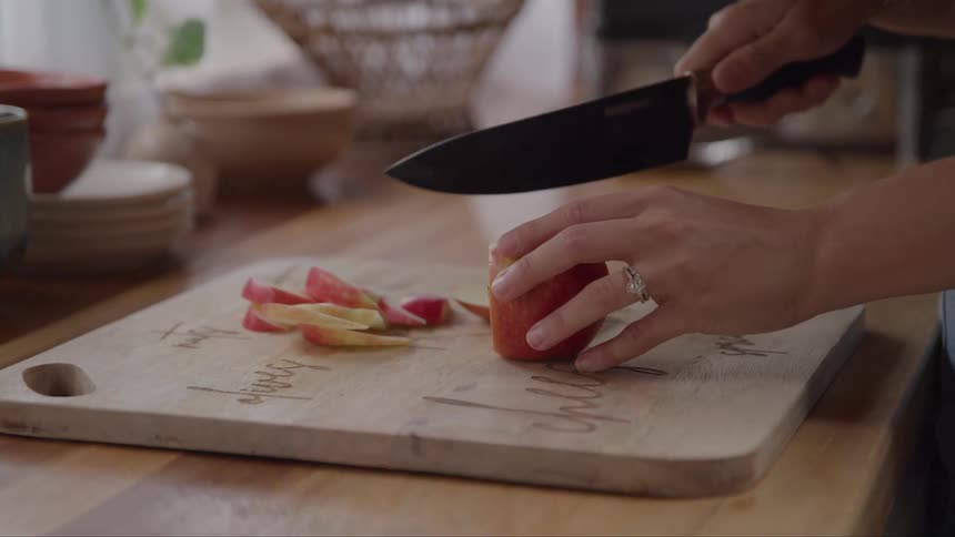 Close up of a woman slicing a red apple on a chopping board in the kitchen