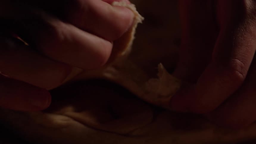 Closeup of hands tearing soft flatbread crumbs catching the warm light