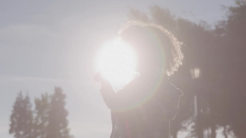 A curlyhaired child blows bubbles outdoors in the sunlight