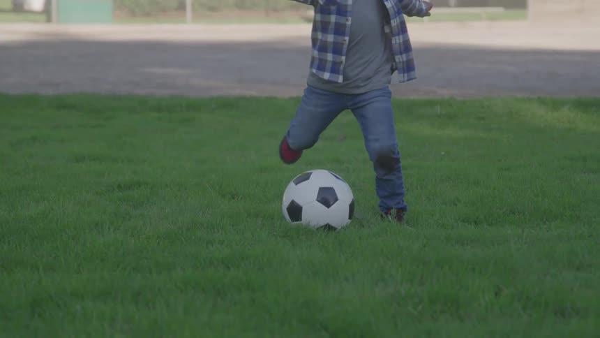 A child in jeans and a plaid shirt kicks a soccer ball on the grass
